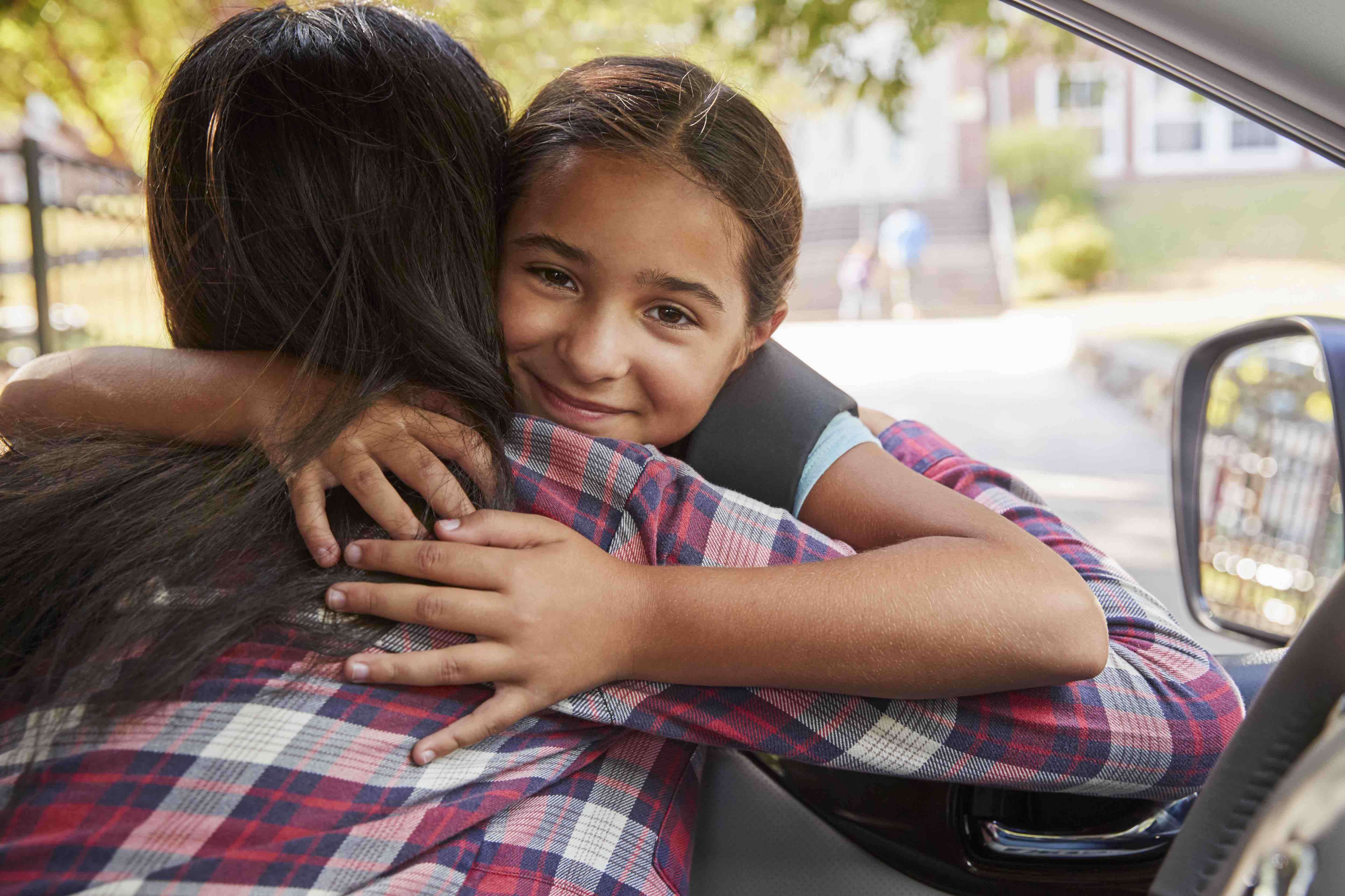 girl hugging an adult through a car window